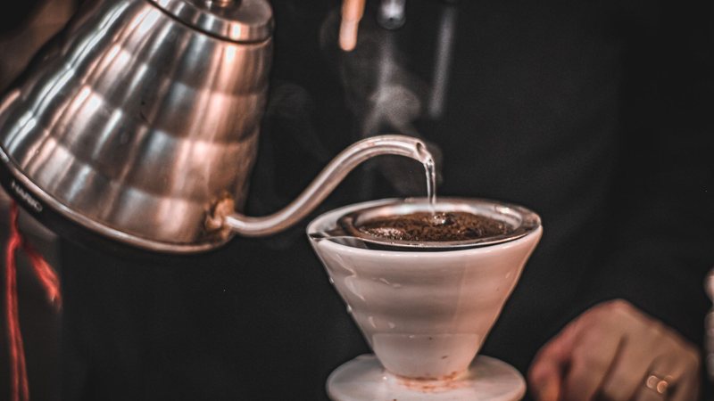 Photograph of hot water being poured from a gooseneck kettle into a pour-over coffee dripper