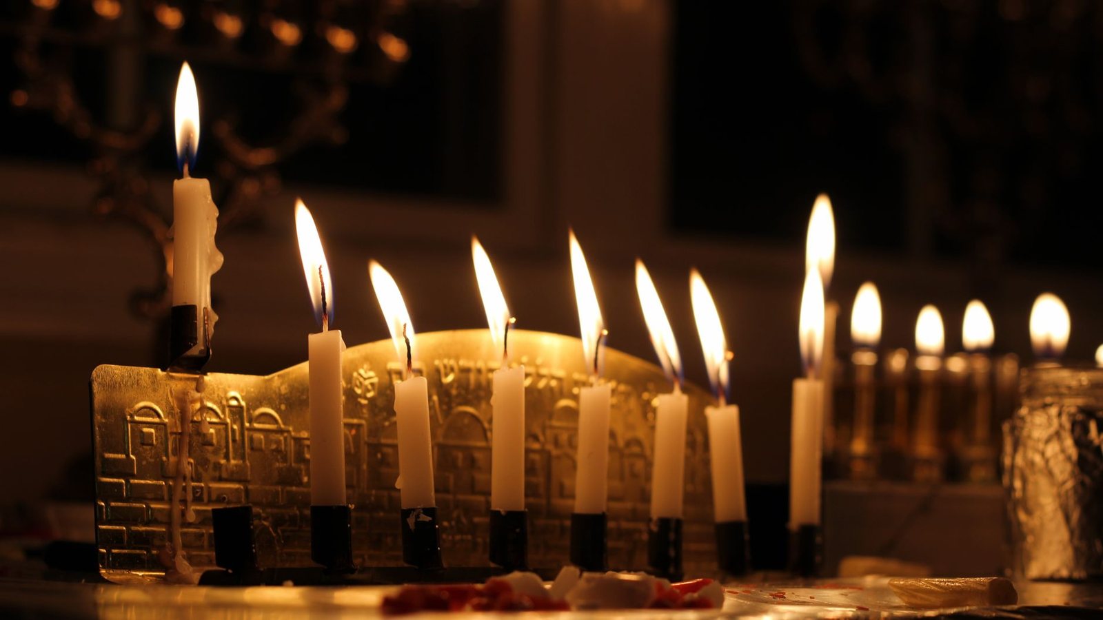 Photograph of a row of lit Chanukah menorah candles glowing in a dark room