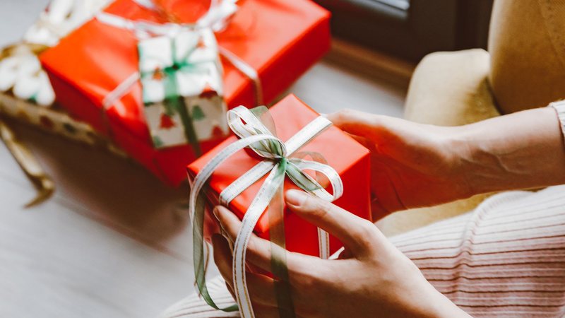 Photograph of hands holding a red gift tied with green and white ribbon