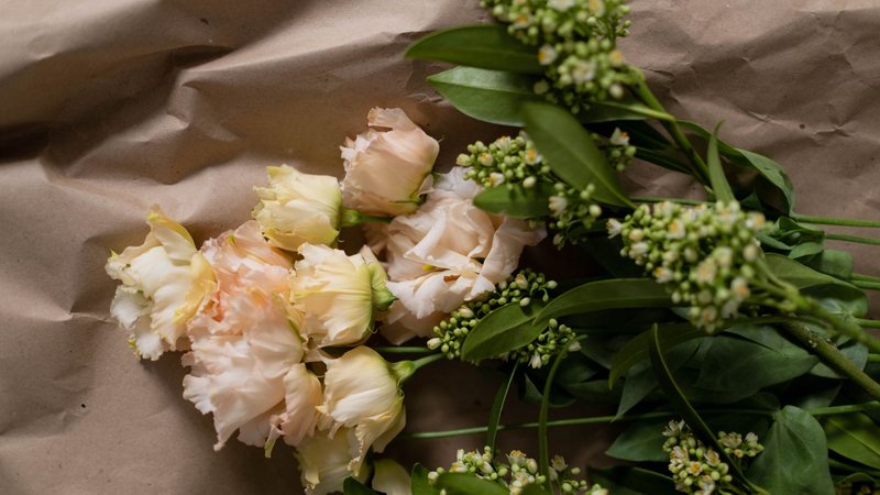Photograph from above of a loose bunch of blush lisianthus flowers and green buds lying on creased brown paper