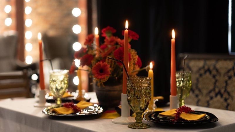 Photograph of a dinner table set with tall candles, red gerberas and amber glassware
