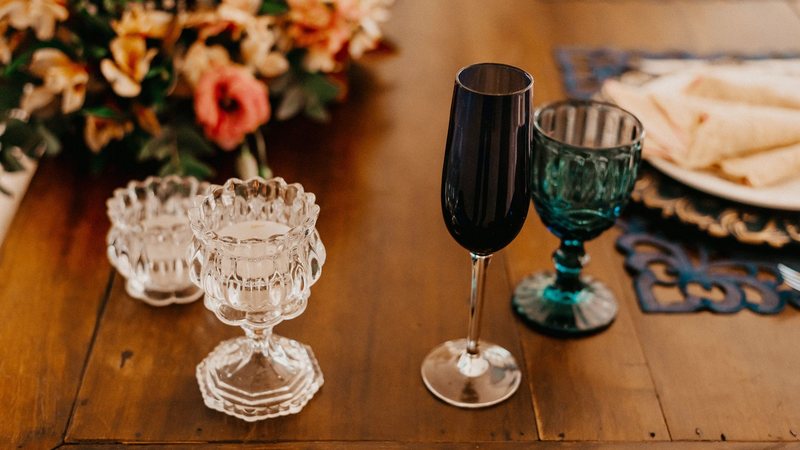 Photograph of a wooden table set with crystal candle holders, wine glasses and a peach and coral flower arrangement